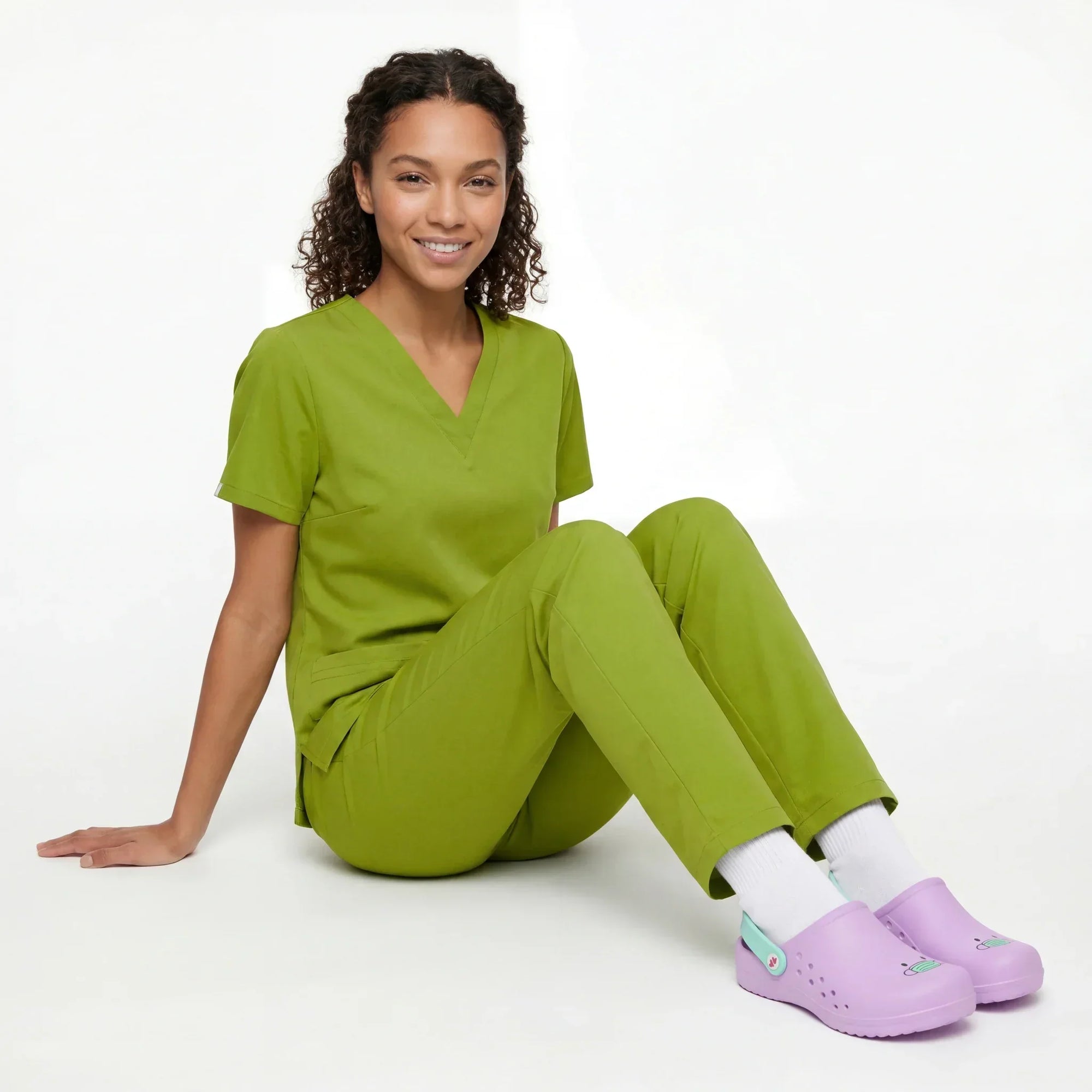 Enfermera sentada en el suelo con zuecos sanitarios verdes y uniforme médico